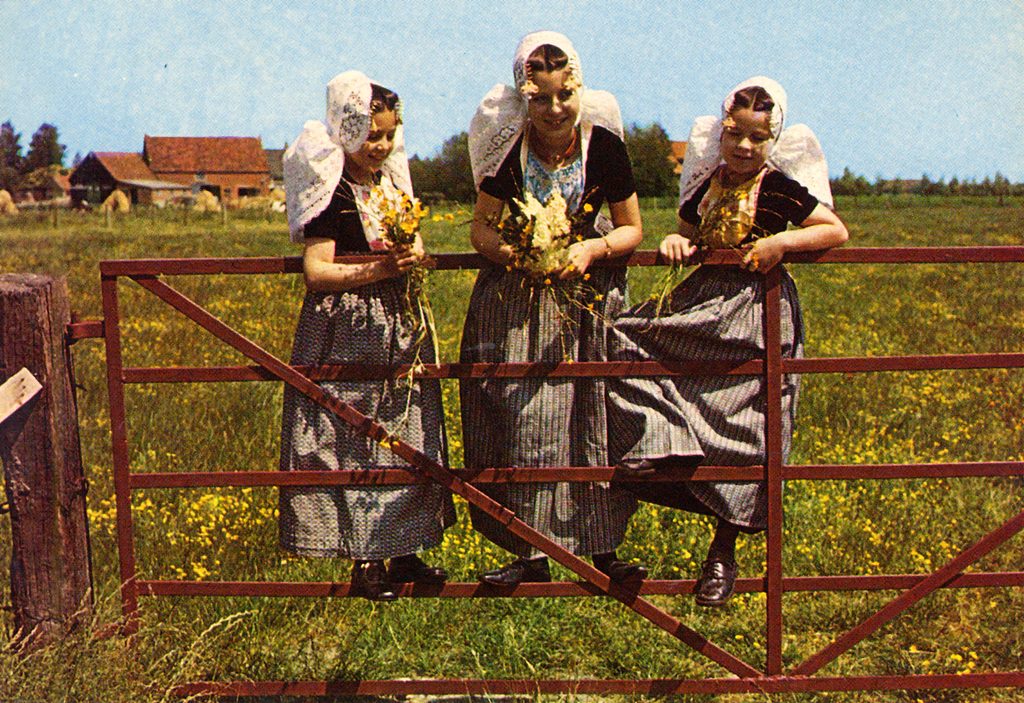 Drie meisjes in Zeeuwse klederdracht op een hek in Zeeland